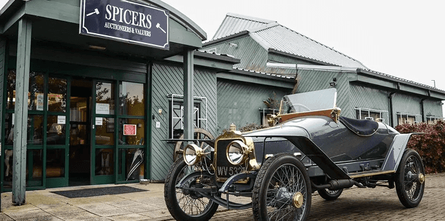 Outside of Spicer's Auction House with a vintage automobile in front.