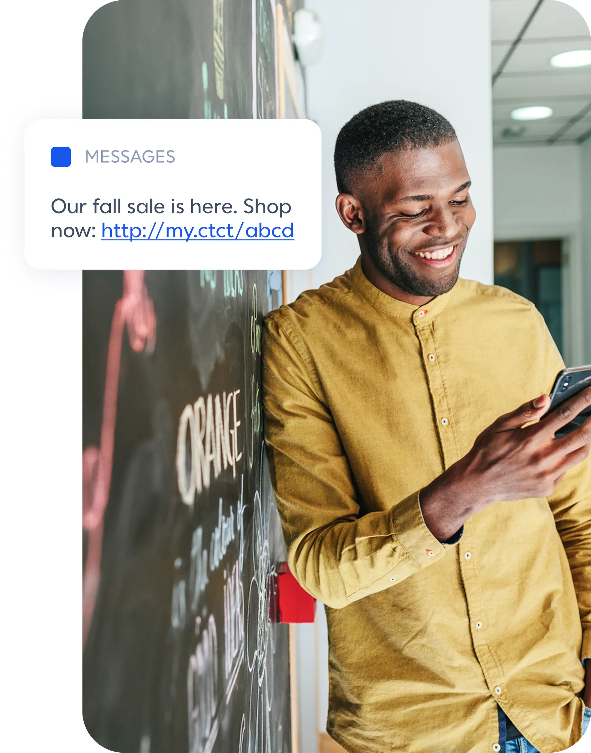 Man leaning against a wall smiling at his phone with a graphic overlay of a text message that reads "Our fall sale is here. Shop now: http://my.ctct/abcd"