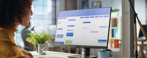 A person seated in front of a computer monitor displaying a calendar.