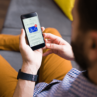 A man sitting on a sofa looks at email on his smartphone.