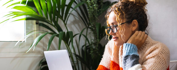 A woman sits in front of a laptop with a mug next to her.