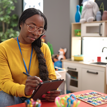 A woman with a clipboard sits at a table surrounded by toys.