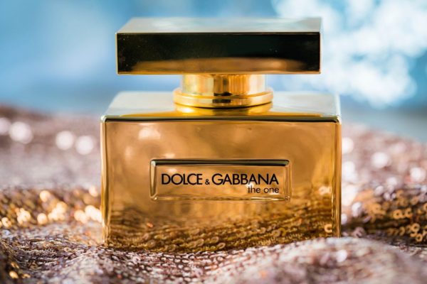 product beauty shot of a shiny bottle of Dolce & Gabbana "the one" set on a bed of sequined fabric