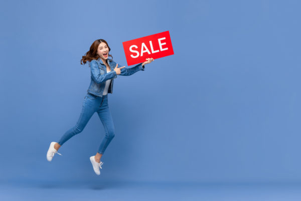 Woman holding a sale promotion sign and jumping in the air with joy