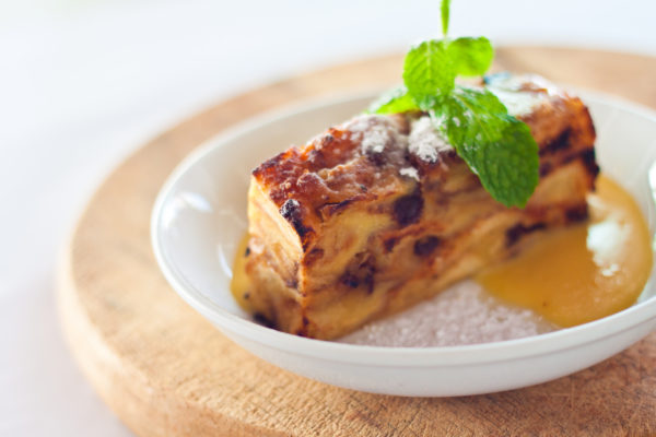 every restaurant website design should include professional photographs of the restaurants own food, like this image of bread-and-butter pudding topped with powdered sugar and a sprig of mint