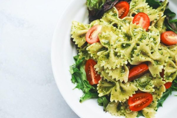 bow tie pasta with pesto and roma tomatoes on a bed of lettuce, served on a white dish