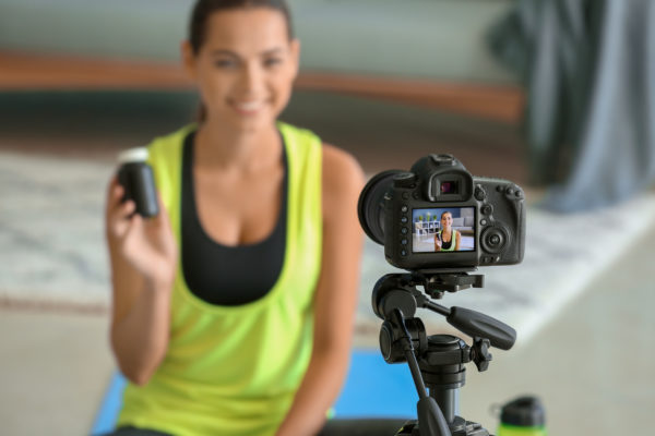 How To Market Health Supplements - Use social media to show off your health supplement like this woman in gym clothes recording a video and holding a bottle of supplements up so the camera can see it