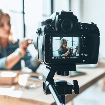 A woman sitting at a table is filmed with a digital video camera.
