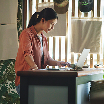 A woman sits behind a desk in a home office looking into a laptop.