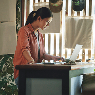 A woman sits behind a desk in a home office looking into a laptop.