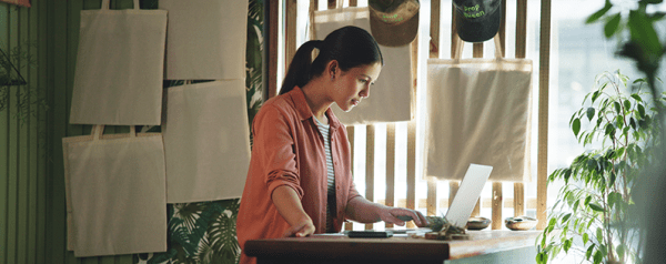 A woman sits behind a desk in a home office looking into a laptop.