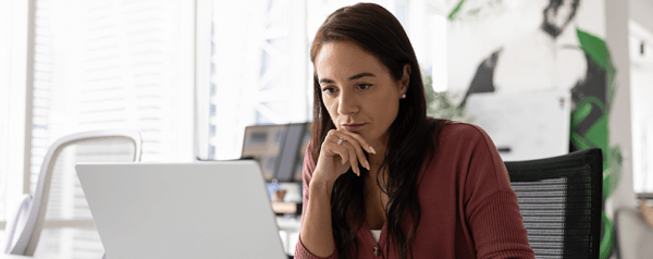 A woman seated at desk looks into her laptop screen.
