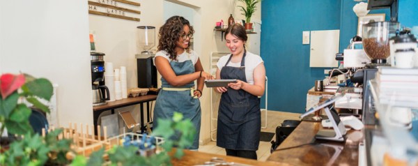 Two women in aprons look at a tablet.