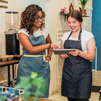 Two women in aprons look at a tablet.