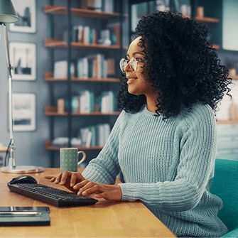 A woman sits at her desk and types a query into an AI search engine on her desktop computer.