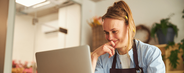 A person in an apron sits in front of a laptop looking at the screen.