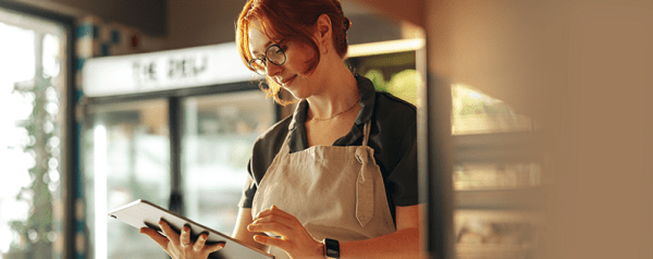 A woman in an apron looks down at a tablet.