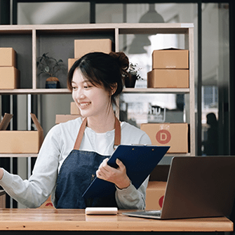 A woman holding a clipboard surrounded by a laptop and