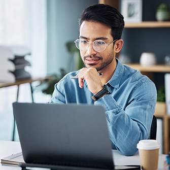A man with glasses sits in front of a laptop.