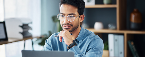 A man with glasses sits in front of a laptop.