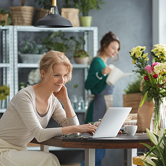 Two women in a flower shop, one standing, one at laptop look at email click-through rates
