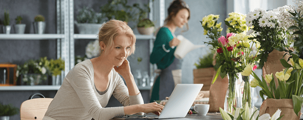 Two women in a flower shop, one standing, one at laptop look at email click-through rates
