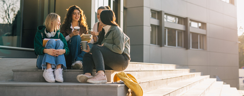 Higher Ed Header College students sitting on the front steps of a higher education institution.