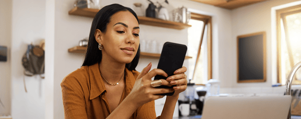 A woman holding a smartphone sits in front of a laptop.