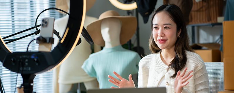 Instagram for Business blog header A woman sits in front of clothed mannequins in her office to film a social media video. Her phone is on a ring light tripod.