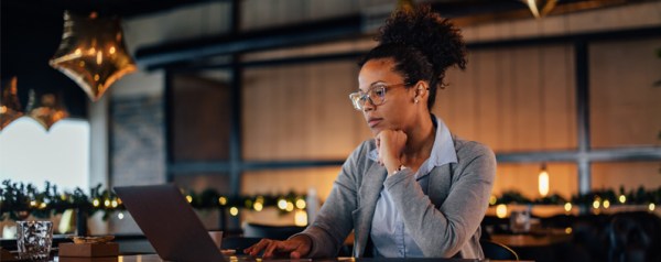 A Black businesswoman works on a computer in an empty restaurant.
