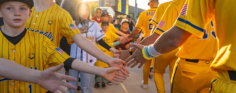 Header_SavannahBanana A baseball player high fiving waiting fans