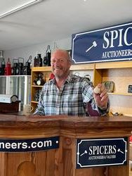 Headshot of Andy Spicer, owner, standing behind the auction podium with a gavel in hand, smiling at the camera.