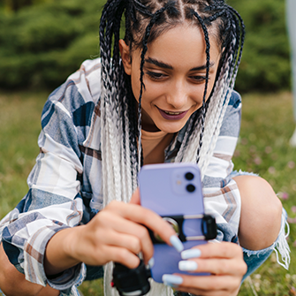 A woman in a field wearing a plaid shirt looks at her smartphone.