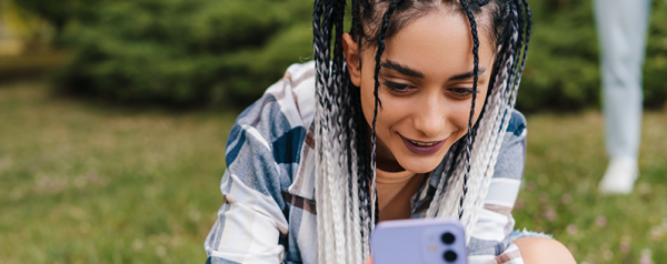 A woman in a field wearing a plaid shirt looks at her smartphone.