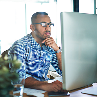 A man wearing glasses sits in front of a desktop computer.