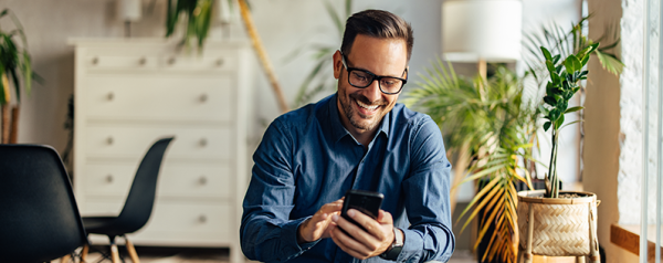 A smiling man holding a smartphone kneels on the floor.