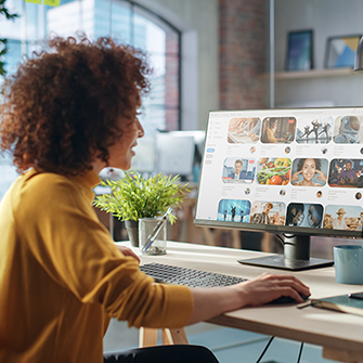 A woman seated at a desk scrolls through images on a computer monitor.