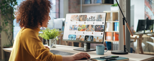 A woman seated at a desk scrolls through images on a computer monitor.
