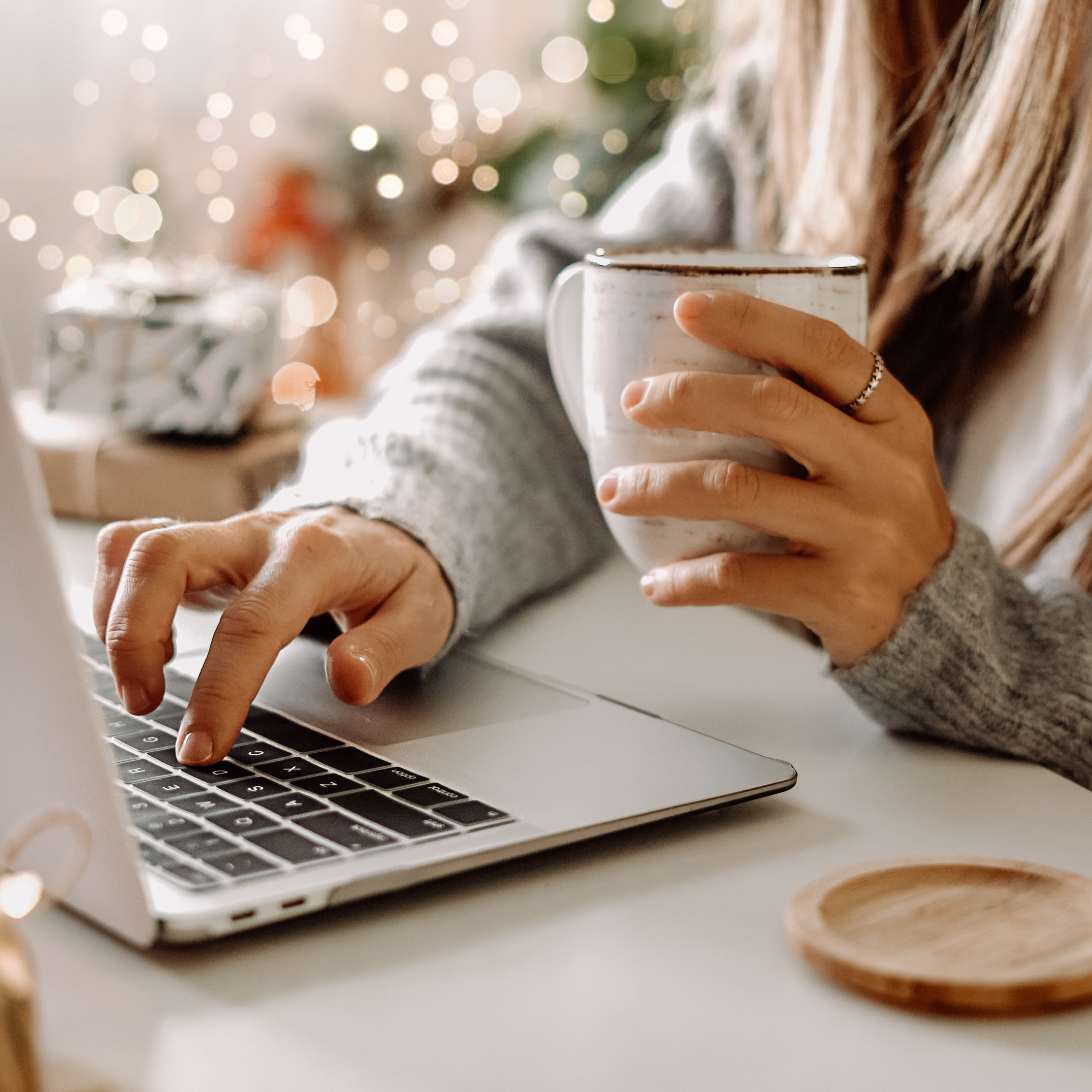 A person sitting in front of a laptop holds a coffee cup in one hand and types with the other.
