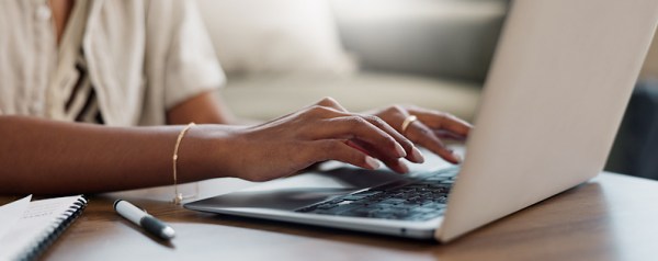 Close-up of a woman's hands typing on a laptop in her home office