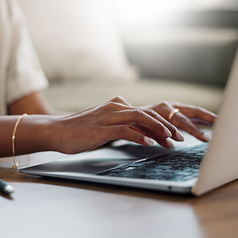 Close-up of a woman's hands typing on a laptop in her home office