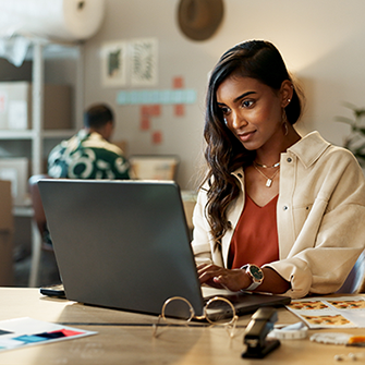 A woman in a home office sits at a laptop looking into the screen.