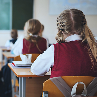 Children wearing uniforms sit at desks in a classroom.