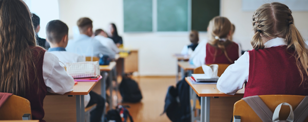 Children wearing uniforms sit at desks in a classroom.