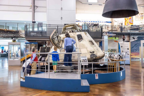A museum visitors stands closely around the Apollo 7 capsule inside the Frontiers of Flight Museum.