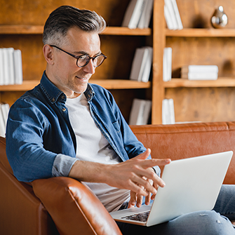 A person sits on a sofa in front of bookshelves looking into a laptop.
