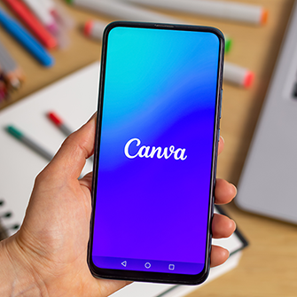 A person holds a smartphone displaying the Canva logo.
