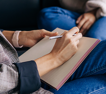 Two people sit across from each other as one writes on a notepad.