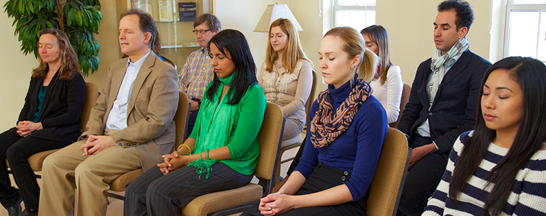A group of people seated in chairs practice the TM technique.