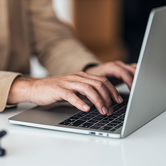 Hands type on a laptop sitting on a white desk.